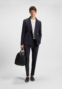 Marine gestreifter, doppelt geknöpfter Anzug mit slim fit, weißem T-Shirt und schwarzen Slippern. Schwarze Tasche mit runder Form und Oberhandgriff.