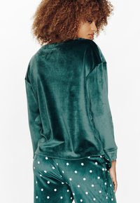 Maglietta verde in velluto a manica lunga con una vestibilità comoda e collo rotondo, abbinata a pantaloni con pois verdi. Tessuto morbido e design rilassato.