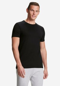 Zwart t-shirt met korte mouwen van zachte stof, met een ronde halslijn en een aansluitende snit. Draag het met grijze trainingsbroek.