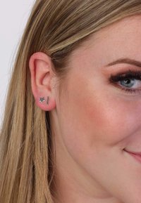 Boucles d'oreilles en argent avec un design en étoile et une barre droite, posées sur un teint clair avec des cheveux blonds raides.
