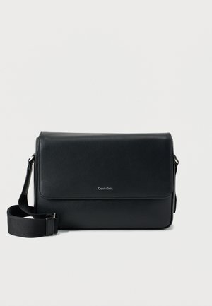Čierna kožená messenger taška s textúrovaným povrchom, nastaviteľným popruhom a predným klopou s jemným logom. Kompaktný a obdĺžnikový tvar.