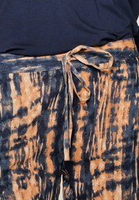 Lekkie, zwiewne spodnie w niebiesko-pomarańczowy wzór tie-dye z detalem wiązania w pasie i teksturowanym materiałem.