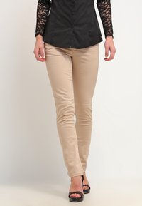 Beige tajta byxor i ett stretchigt tyg, med en slät yta och en figurnära design, parat med svarta sandaletter med remmar.