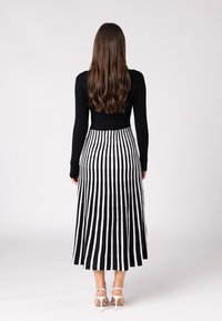 Haut noir à manches longues associé à une jupe maxi rayée blanche et noire. La jupe présente des rayures verticales et une coupe évasée. Sandales blanches.