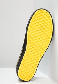 Musta urheilukenkien pohja, jossa on teksturoitu keltainen kumipohja, joka esittelee timanttikuviota pidon ja vakauden parantamiseksi.