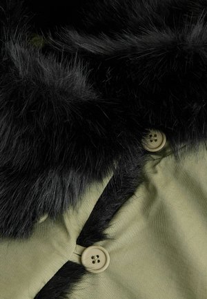 Oliwkowa kurtka z czarnym, sztucznym kołnierzem z futra, z beżowym guzikiem z czterema otworami i gładką tkaniną.