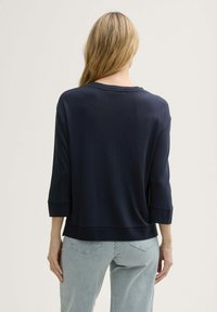 Marineblauw, los-fitting 3/4 mouwen top met een ronde hals en zachte textuur, gecombineerd met licht gestreepte broek.