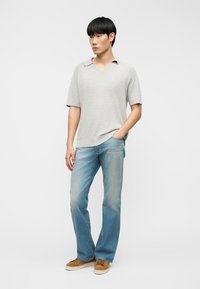 Ανοιχτό γκρι πόλο μπλουζάκι με κοντό μανίκι, συνδυασμένο με ξεθωριασμένο μπλε τζιν παντελόνι σε ίσια γραμμή και καφέ παπούτσια με κορδόνια, σε ουδέτερο φόντο.