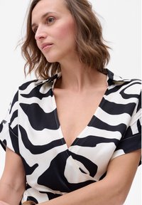 Zwart-wit zebraprint wikkeljurk met een diepe V-hals, korte mouwen en een zachte textuur. Opvallende stikselaccenten langs de randen.