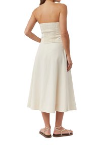 Kremowa sukienka bez ramiączek z marszczonym torsem i rozkloszowanym dołem, w połączeniu z jasnobrązowymi płaskimi sandałami z paskiem w kostce.