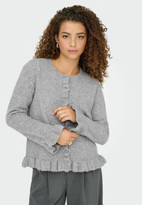 Gilet tricoté gris avec un col rond, fermeture à boutons et ourlet à volants. Texture douce et manches longues avec poignets à volants.
