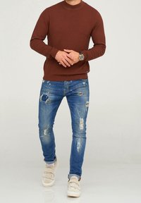 Brun texturerad tröja, prydd med rund hals. Bärs tillsammans med ljusblå ripped jeans och beige sneakers med kardborreband.