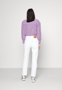 Pantalones blancos ajustados con corte recto, combinados con una camisa de cuadros morada. Un notable parche de cuero en la cinturilla añade detalle.