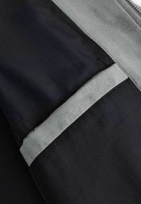 Détail de tissu noir avec une bande horizontale en suède gris et un bord gris, montrant un contraste textile lisse et texturé.