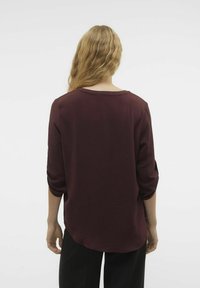 Top lungo bordeaux a maniche lunghe con vestibilità comoda, tessuto testurizzato e scollatura a barchetta. Presenta maniche arrotolate e orlo curvo.