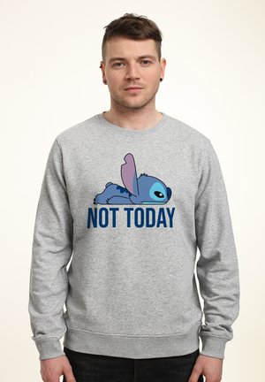 Mann trägt grauen Pullover mit einer blauen Cartoonfigur, die oberhalb des Textes „NOT TODAY“ auf einem einfarbigen Hintergrund liegt.