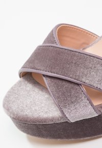 Sandale plateforme en velours violet doux avec des brides croisées et un intérieur beige lisse. Dispose d'une semelle épaisse, texturée et douce.