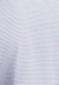 Shirtstof met een klein, herhalend ruitpatroon in marineblauw en lichtblauw op een witte achtergrond, met een zachte textuur.