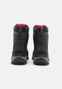 Bottes imperméables noires avec doublure rouge, support de cheville haut, panneaux latéraux texturés et logo sur le talon. Semelles en caoutchouc durables pour une meilleure adhérence.