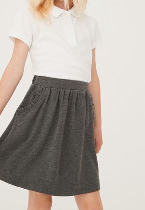 Enfant portant un polo blanc à manches courtes et une jupe gris foncé avec une taille froncée et des détails de poches à volants.
