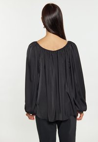 Musta pitkähihais blouse, jossa on laaja kaula-aukko ja kerätty kangasdetail. Silkkinen ja virtaava satiinituntu, rento istuvuus. Muotoillut hihansuut.