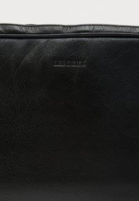 Czarna skórzana torba o fakturowanej powierzchni z subtelnym wytłoczonym logo "LES DEUX". Kompaktowy design z gładkim zamkiem błyskawicznym.