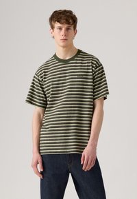 Camiseta às riscas em verde e creme, com um corte descontraído, gola redonda canelada e mangas curtas. Tecido texturado com uma marcação subtil.