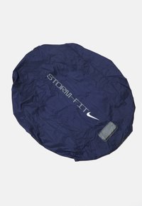 Housse de pluie ronde bleu marine avec une texture plissée, marquage "STORM-FIT" en gris clair et une petite poche rectangulaire sur le côté.