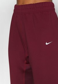 Burgundy workout pants with an elastic waistband, featuring red stitching and a small silver Nike logo on the left side.