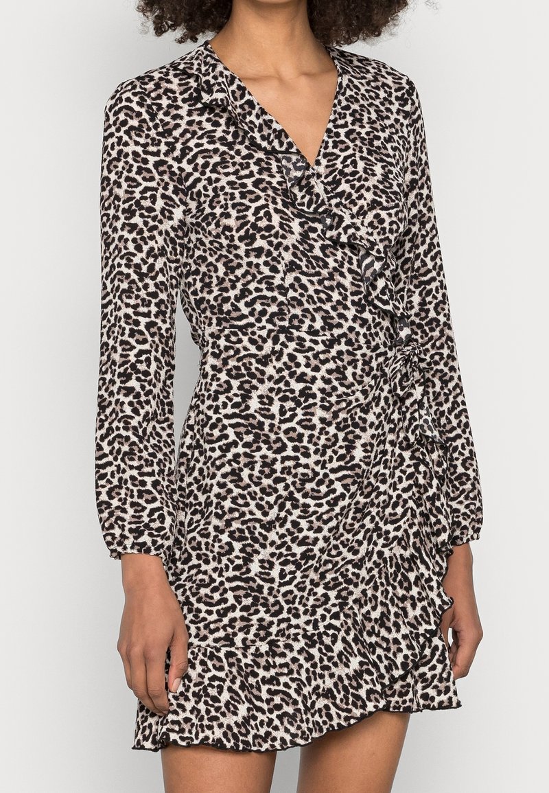 Kobieta w długiej, leopardo wzorzystej sukience z długim rękawem, z falbanami wzdłuż dekoltu, talii i dolnej krawędzi.