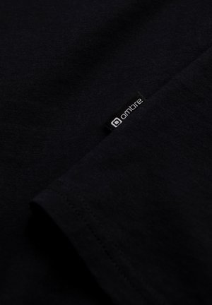 Czarna koszulka z miękkiej bawełny, o gładkiej fakturze, z małą metką z logo "ombre" na dolnym wykończeniu.
