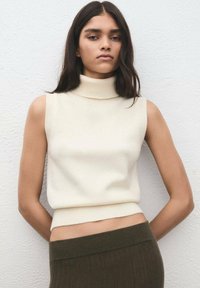 Top crem fără mâneci, cu guler mock-neck, fabricat dintr-un tricot moale, având talie ajustată și accente cu model striat. Fundalul este neutru.