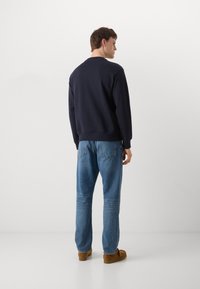 Sudadera azul marino con cuello redondo, puños y dobladillo de canalé, combinada con jeans azul claro y zapatos de ante marrón.