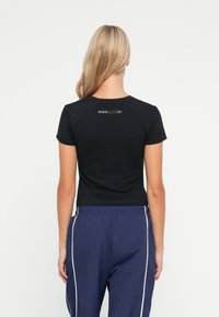 Černé tričko s krátkým rukávem a kulatým výstřihem. Obsahuje malou černou visačku s logem Nike na horní části zad. Vyrobeno z hladké, elastické tkaniny.