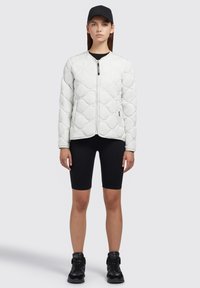 Vatteret hvid jakke med en tætsiddende design, lynlåslukning og rund hals, parret med sorte ribbede cykelshorts og sorte sneakers.