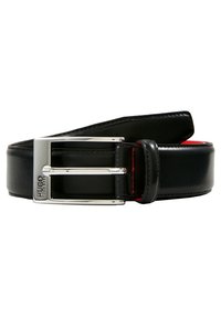 Cinturón de cuero negro con una hebilla de plata pulida, que presenta costuras rojas a lo largo de los bordes. La hebilla es rectangular y tiene un logotipo.