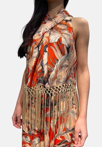 Abito senza maniche a fantasia floreale in arancione e beige, con rifinitura dorata a frange in vita. Tessuto dalla texture morbida con design drappeggiato.