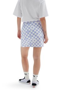 Jupe à carreaux bleu et blanc avec motifs floraux, en tissu, associée à des baskets Vans noires et des chaussettes blanches avec logo.