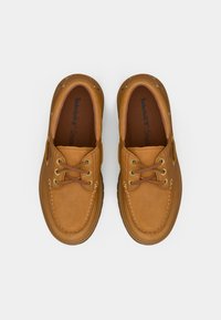 Brune lærbådsko med brune snørebånd, metal øjer og polstret krave. Indersålen har Timberland-logo.