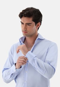 Camicia azzurro chiaro con colletto aperto, maniche lunghe e polsi con bottoni. Il tessuto presenta una texture liscia e una leggera lucentezza.