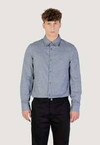 Camicia a bottoni azzurro chiaro con una sottile trama, maniche lunghe e colletto. Abbinata a pantaloni neri, che mostrano uno stile semplice e classico.