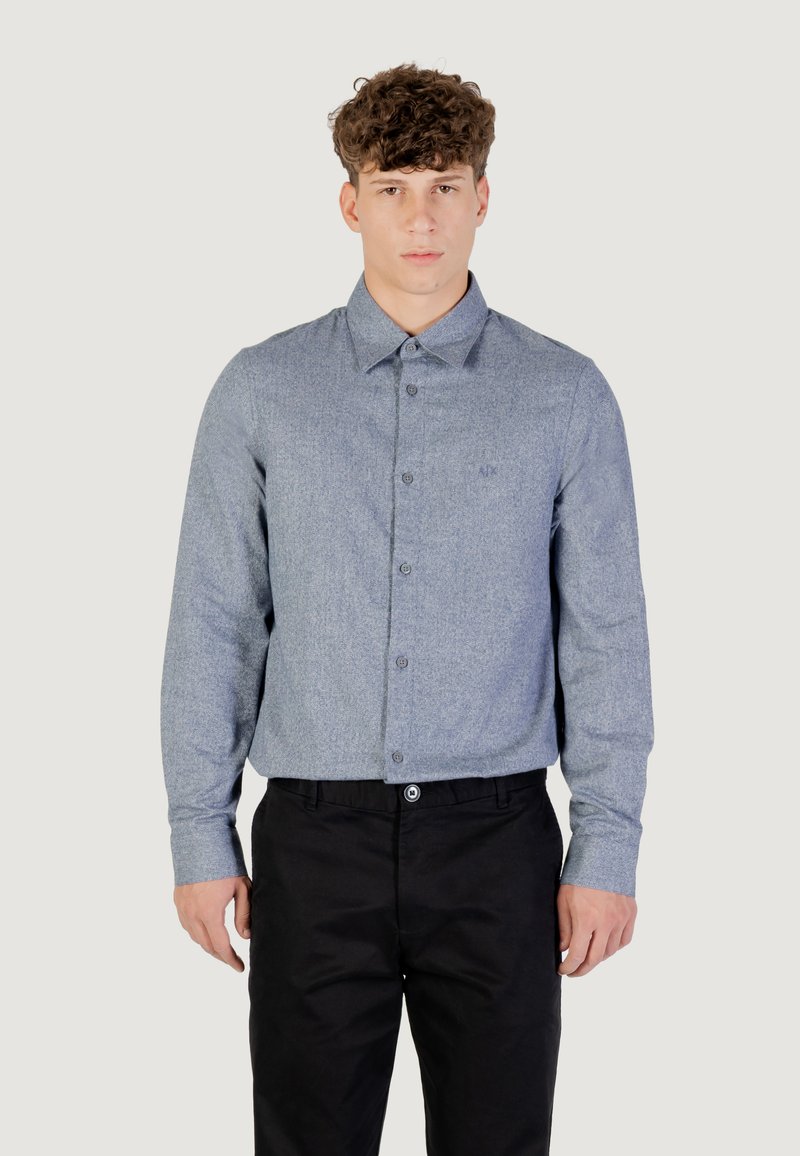 Camicia a bottoni azzurro chiaro con una sottile trama, maniche lunghe e colletto. Abbinata a pantaloni neri, che mostrano uno stile semplice e classico.