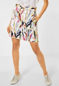 Värikäs kuviollinen hame valkoisella taustalla, jossa on vihreitä, vaaleanpunaisia ja mustia abstrakteja kuvioita, joustava vyötärö ja napituskoristeet.