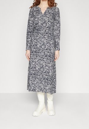 Woman wearing a long-sleeve, black and white zebra print midi dress with a V-neck, paired with white knee-high chunky boots.
