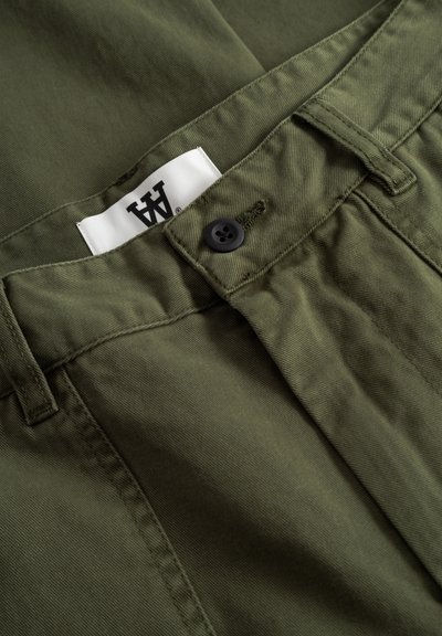 Pantalon en coton vert olive avec une texture lisse, doté d'un bouton noir et d'une étiquette blanche avec un logo noir près de la ceinture.