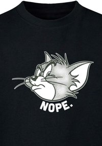 Melnas kokvilnas T-krekls ar grafiku, kurā attēlots karikatūras kaķa galva ar pārspīlētu izteiksmi un baltiem burtiem apakšā "NOPE."