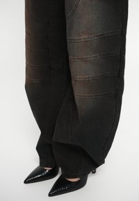 Črne široke jeans hlače s plastenimi šivi; v kombinaciji z črnimi patentnimi usnjenimi petami z vzorcem krokodila.