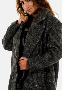 Cappotto in lana grigia con motivo a spina di pesce, design oversize, colletto a punta, due grandi bottoni e tasche laterali. Tessuto testurizzato e vestibilità rilassata.