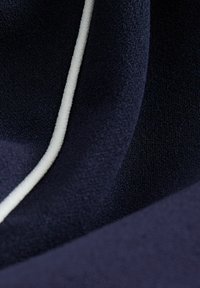 Tmavomodrá tkanina s jemnou textúrou, s bielou akcentovou linkou. Povrch má mierny lesk a jemné variácie textúry.