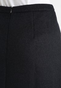 Sort uldnederdel med en tekstureret finish, der har en diskret lynlås og en skræddersyet pasform. Rene linjer og minimalistisk design.